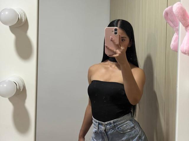 LaurentRay with long black hair, wearing a black strapless top and high-waisted blue jeans, taking a mirror selfie with a pink phone, showing her tits and slim ass.