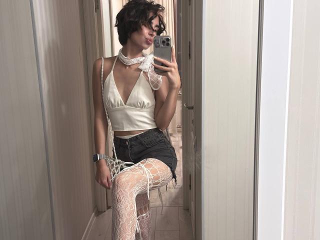 TameikaMacclellan with short dark hair, white lace choker, satin bralette, black denim shorts, white lace stockings, and a silver bracelet, taking a mirror selfie.