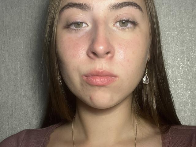 LashawnBlady tem pele clara, olhos verdes e cabelo castanho, com pequenas argolas e uma espinha no lábio inferior. Ela está fazendo uma expressão de descontentamento, vestindo uma blusa rosa..