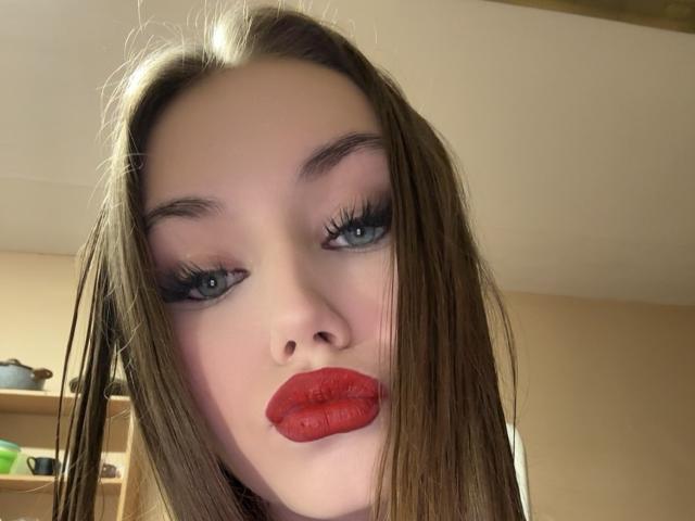 CaritaShover's face, pale skin, blue eyes, long brown hair, red lipstick, and thick black eyelashes. Boobs not visible, focus on her pouty lips and makeup.