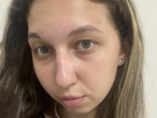 Sanella has a slightly shiny, pale skin face with small nose, brown eyebrows, gray eyes, and light brown hair with blonde highlights. She's wearing a pearl earring and black top.