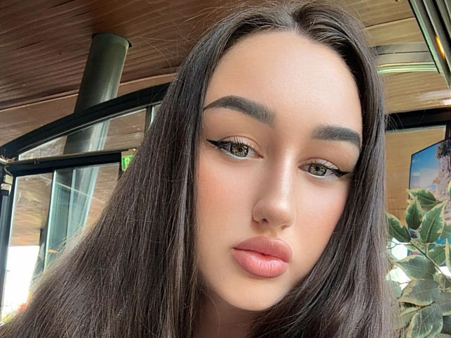 FortuneX heeft lang, recht bruin haar, groene ogen en lichtroze lippen met opvallende eyeliner. Haar gezicht is recht vooruit gericht, waarbij haar neus en licht openstaande, roze lippen zichtbaar zijn..