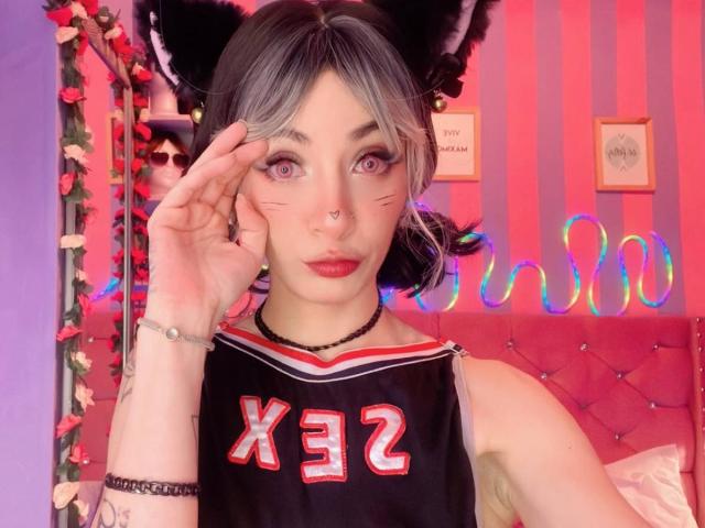 LaurenEvie69 com orelhas de gato, cabelo preto e cinza, batom vermelho, colar preto, piercing no nariz e top esportivo preto X3Z, tocando o rosto com olhos rosa, fofa e sexy..