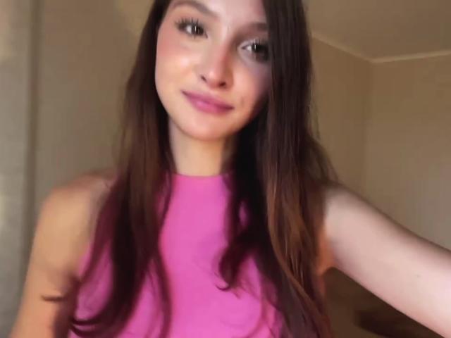 Kassandra Dalal, avec ses longs cheveux bruns, son haut rose et son sourire discret, montrant sa petite poitrine et son joli visage, sur une photo de profil légèrement floue..