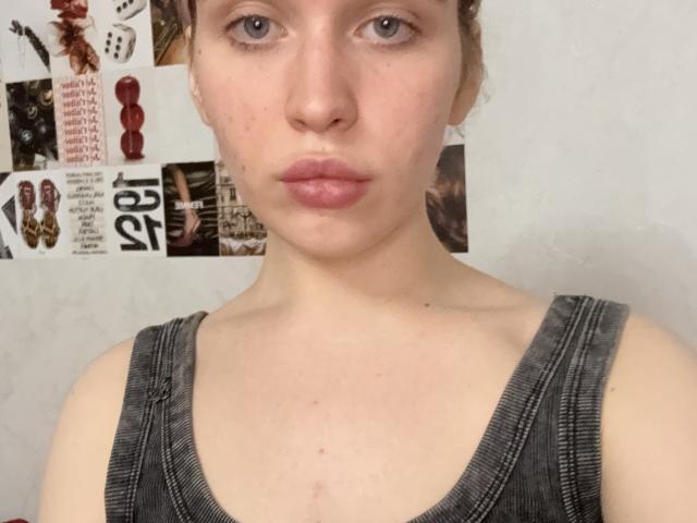 HazelPereyda a la peau pâle, les yeux bleus et les lèvres roses. Elle porte un débardeur gris qui révèle ses petites seins et ses taches de rousseur. Son expression est neutre, et elle regarde l'appareil photo..