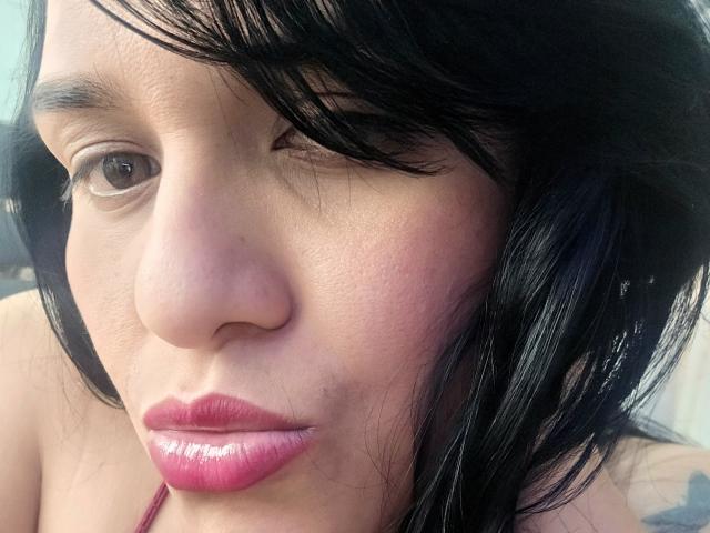 O rosto de Viviana Thompson, com batom rosa brilhante, lábios levemente entreabertos, olhos castanhos e cabelo preto ondulado cobrindo um olho. Seu nariz é pequeno e sua pele é de cor marrom clara..