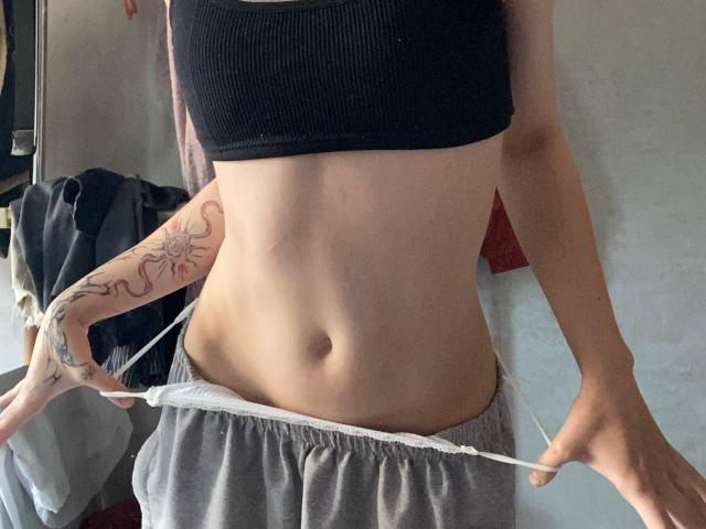 KarlaRolison's bare midriff with small tits, black ribbed crop top, gray sweatpants pulled down, showing her white waistband. She has a sun tattoo on her left arm.
