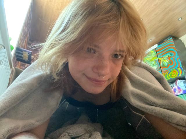 KarlaRolison has blonde, messy hair, a nose ring, and a slight smile, wearing a gray blanket over a black top, with her small tits visible.