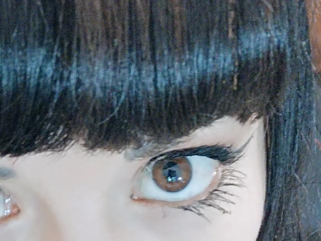 OrianaLaFrancaise's brown eye with thick black eyelashes and straight dark brown bangs, showing her pale skin and slight eye reflection. Her eye is looking directly at the camera.
