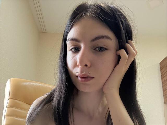 NobukoGraue heeft lang zwart haar, een neusring en een lipring, met haar hand op haar wang, met een neutrale uitdrukking en lichte make-up, op een selfie..
