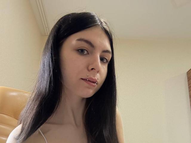 NobukoGraue ha lunghi capelli neri, un piercing al naso e un piercing al labbro. Sta guardando la fotocamera con un leggero sorriso, indossando una maglietta bianca..