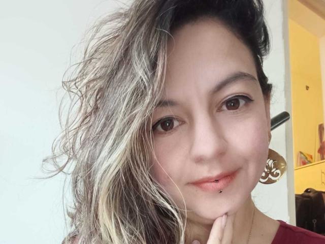 ArianaBlonde tiene el cabello rubio y castaño, con un aspecto despeinado, ojos marrones y un piercing en el labio inferior derecho. Lleva una camisa roja y aretes dorados..