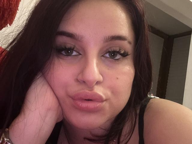 Luucie's pouty face with glossy pink lips, brown eyes, and dark brown hair. She's resting her cheek on her hand, showing a small beauty mark on her left cheek.