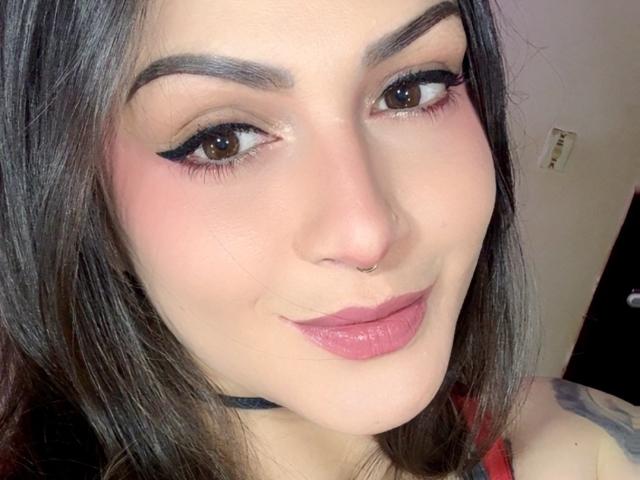 ElinaJhonson has dark hair, brown eyes, black winged eyeliner, pink blush, pink lipstick, nose ring, and a subtle smile, with a black choker visible on her neck.