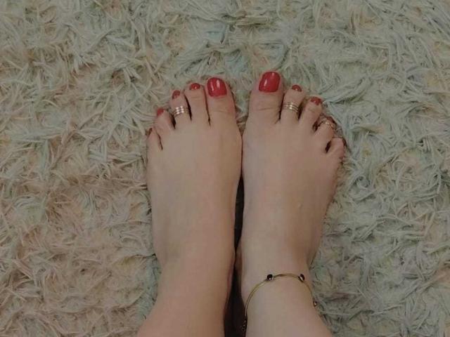 I piedi nudi di VittoriaI, con le unghie dei piedi dipinte di rosso, gli anelli dorati alle dita dei piedi e un braccialetto dorato alla caviglia, poggiati su un soffice tappeto bianco..