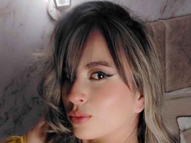 AmiiRosse hat ein süßes Gesicht mit blonden und schwarzen Haaren, schwarzem Eyeliner und rosafarbenen Lippen und blickt mit einem leichten Lächeln in die Kamera. Ihre Nase ist klein und ihre Haut ist hell..