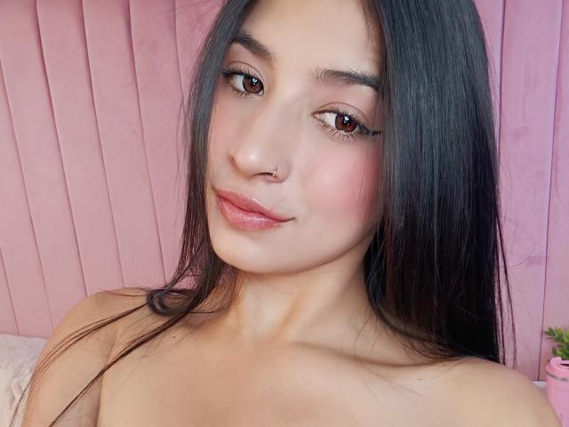 NaiaSanders heeft lang zwart haar, bruine ogen, roze lippen, een neusring, en is naakt met gladde, lichte huid, waarbij haar borsten en een subtiele roze tint zichtbaar zijn..