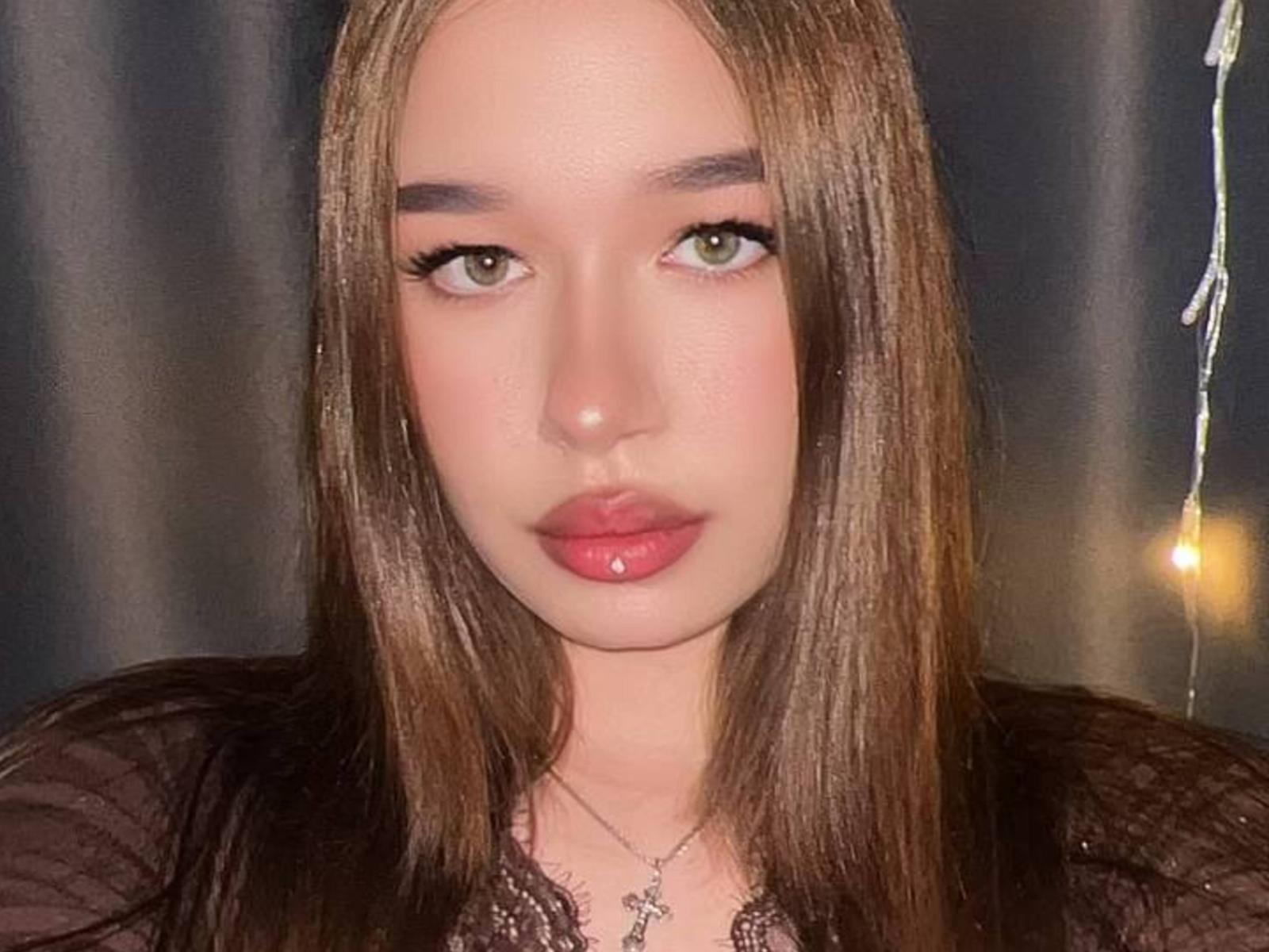 Arcelia Carmody tiene el pelo largo y castaño, ojos verdes y labios rojos. Lleva una blusa negra transparente y un collar de plata con una cruz. Su trasero no es visible..