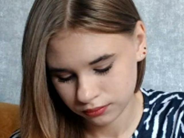 Brittaney Jecklin tem cabelo castanho liso, olhos fechados e batom vermelho, vestindo uma camisa listrada, com brincos discretos, olhando para baixo com um leve sorriso..