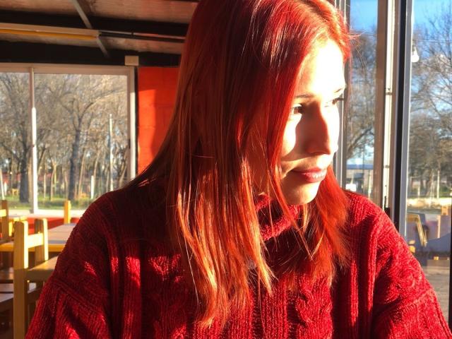 KiaraHernandezX with red hair, sunlit, wearing a red knit sweater, looking to the side, showing a slight pout, medium breasts, and a cute, casual look.