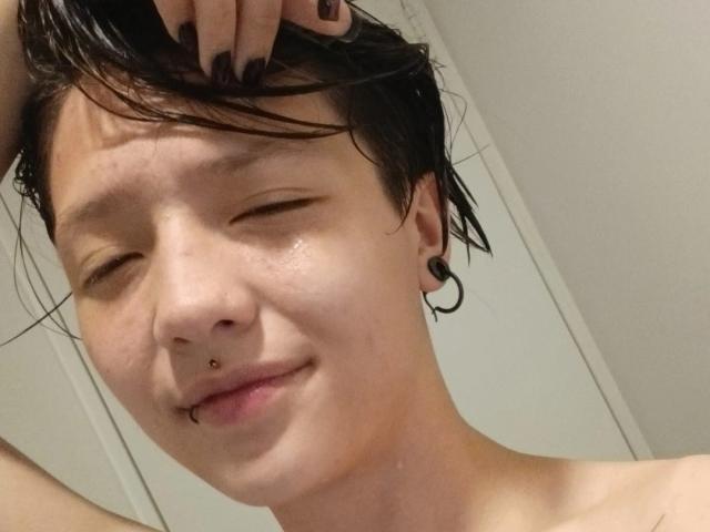 LissyLuxe with wet black hair, nose ring, and black ear gauge, smiling with eyes closed, showing a small lip piercing, and dark nail polish.