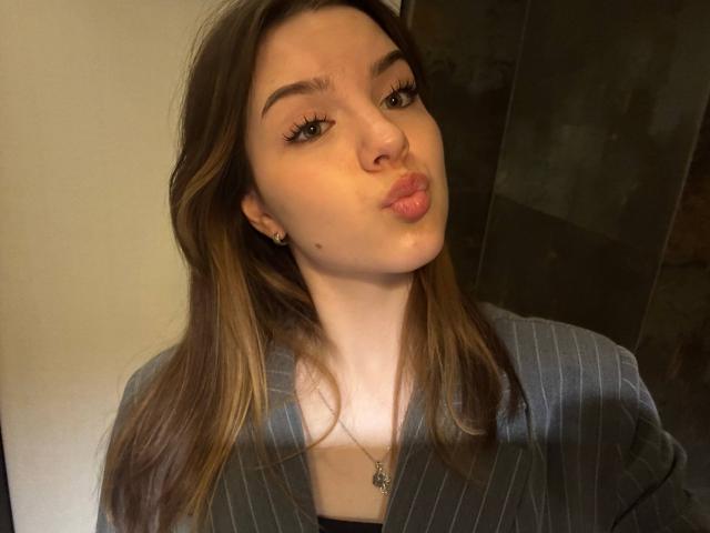 EviaDorland has pouty lips, long brown hair, and wears a striped blue shirt, with a necklace and earrings, looking at the camera. She's got cute, small tits.