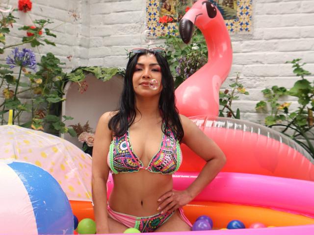 ChanelBrouw, met een gemiddelde borstmaat, donker haar en een bruine huid, draagt een kleurrijke bikini en staat in een opblaasbaar zwembad met een roze flamingo en een strandbal..