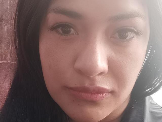 ArianithaXox's face, with dark brown eyes, long black eyelashes, and pink lips, showing light freckles and small moles. She has straight black hair and a neutral expression.