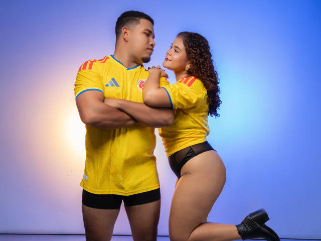 Lucas has a muscular build, wearing a yellow soccer shirt and black shorts, standing with Sasha, who has curly brown hair, a yellow shirt, black panties, and black heels.
