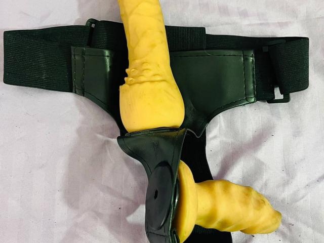 Yellow dildo with ridged texture, strapped to green tactical holster, positioned vertically, with dildo's head pointing downward. CataleyaSweett's dildo is secured in tactical gear.