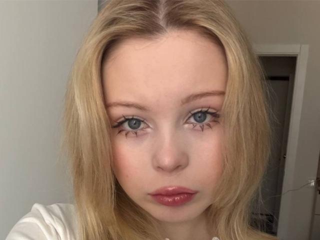 StellaMelow has blonde hair, blue eyes, and pink lipstick with black eyeliner. She's looking directly at the camera with a neutral expression. Her tits are not visible.