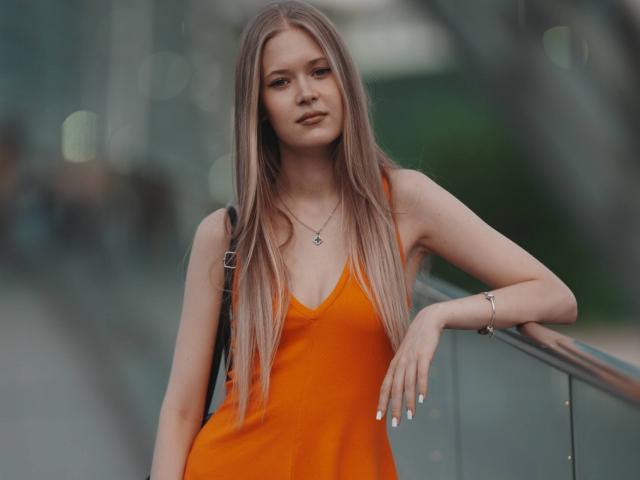 LillianaWhang with long brown hair, orange dress, small tits, leaning on glass railing, silver necklace, bracelet, slight smile, soft light, bokeh background, casual, confident, sexy.