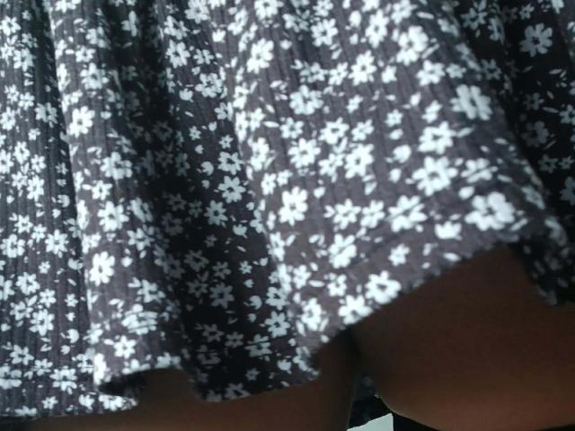 ZarayFeet's skirt, showing dark gray fabric with white floral patterns, slightly lifted to reveal brown thighs. No other visible body parts. Skirt texture is slightly wrinkled.