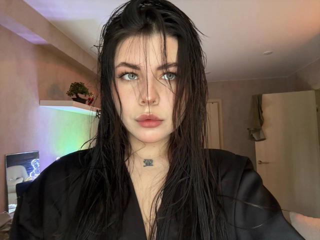 Joey Bickart, avec ses cheveux noirs mouillés, ses yeux bleus et son anneau de nez, portant une robe noire, a un tatouage sous le menton et une expression sérieuse..