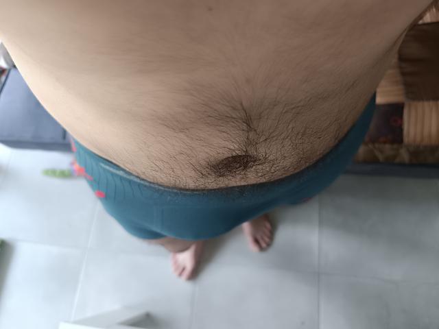 OrianaAndFriends' hairy belly button, surrounded by dark brown pubic hair, in teal underwear, with bare feet on a tiled floor, viewed from above.
