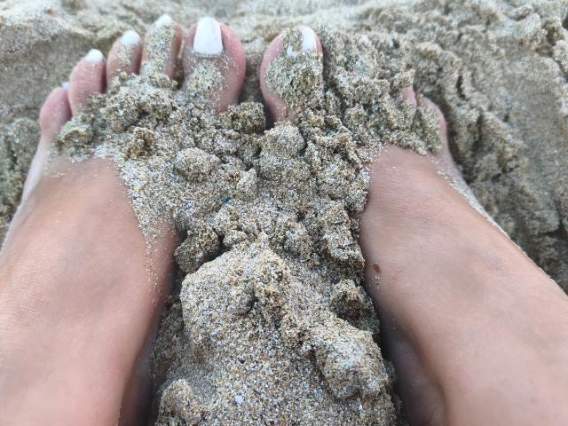 LilithGreenn's sandy-covered feet with white-painted toenails, toes pointing upwards, showing a pile of wet, gritty sand between them.