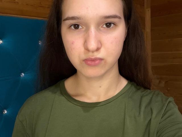 ColbyCupps ha un viso serio, con la pelle chiara, gli occhi marroni e i capelli lunghi castani. Indossa una maglietta verde, e il suo piccolo naso, leggermente rivolto verso l'alto, è visibile..
