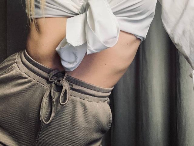 La sezione centrale di BalletSwan mostra una camicia bianca annodata, che rivela un addome piatto, abbinata a pantaloni grigi con un cordoncino. I capelli biondi sono parzialmente visibili sul lato sinistro..