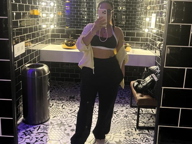 GalaMalkova stands in a black-tiled bathroom, mirror selfie, wearing a white open shirt, black bra, and high-waisted black pants, with a slim, curvy figure, and medium tits.