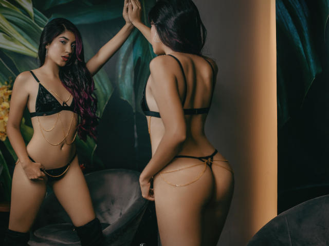 CrystalHadid with long purple-tipped hair, black lace bra, and gold chain lingerie, showing her ass and staring at her reflection, wearing black knee-high boots.