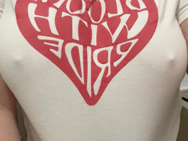 RouseKirryHot's white t-shirt with a red heart graphic shows their sizable, slightly visible, firm boobs. The heart graphic is centered on their chest.