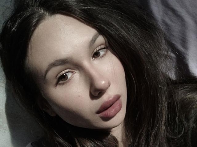 CheryLessly's face, showing pale skin, brown eyes, and full pink lips with slightly parted mouth. Long dark brown hair, looking down with a soft, calm expression.
