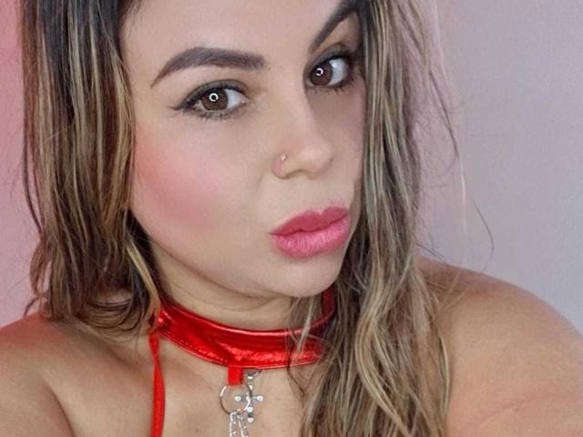 LiaAdams with pink pout, brown eyes, nose piercing, red shiny choker, and blonde hair, looking at camera, showing her tits.