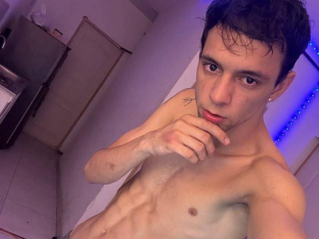 Franchessco69, senza camicia, con capelli scuri e bagnati, occhi marroni e un piccolo tatuaggio sulla spalla destra, che si morde un dito, mostrando un petto esile, tonico e peloso..