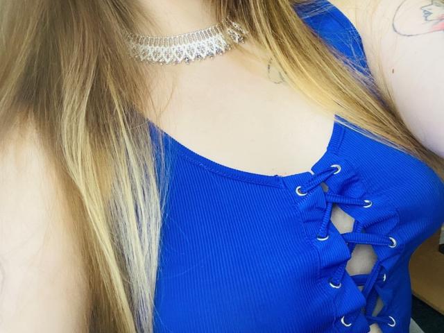 KarKutie's blue ribbed top with lace-up front, showing her tits, and a silver choker necklace, with long blonde hair and a tattoo on her right arm.