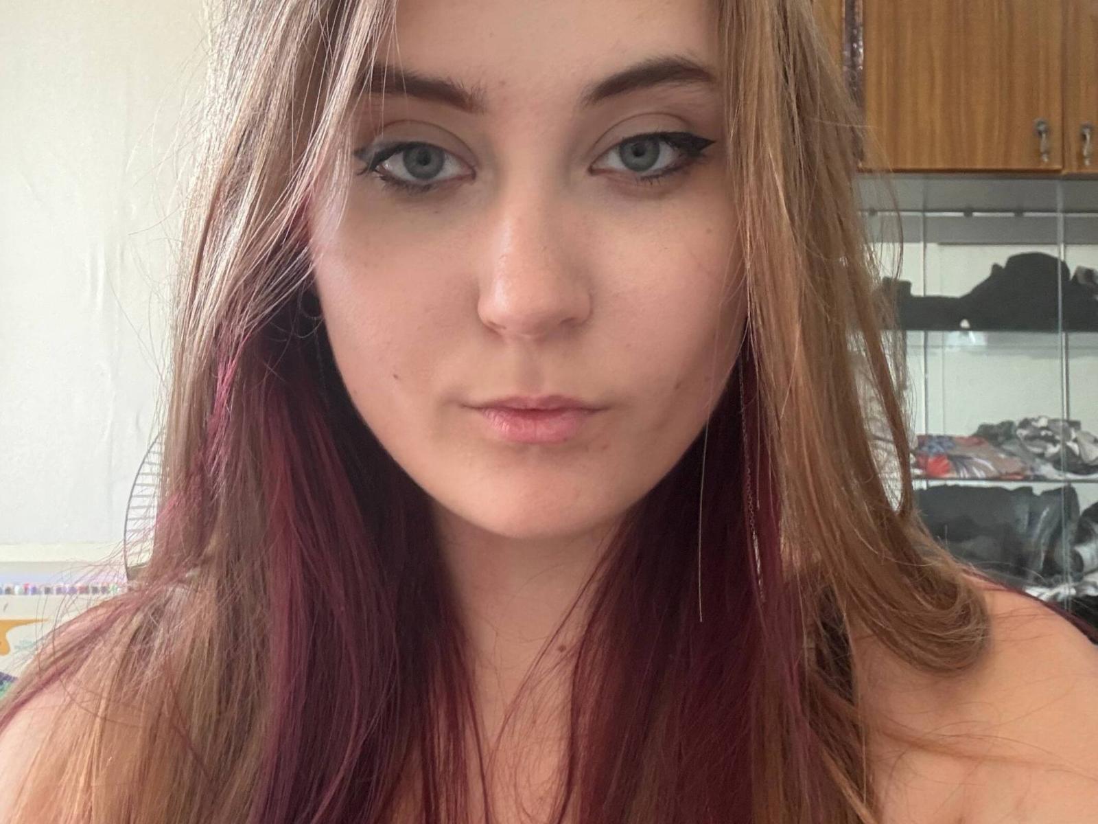 VaniaWaker tem cabelos castanhos longos com pontas vermelhas, olhos azuis e delineador preto. Ela está olhando diretamente para a câmera com uma expressão neutra. Seu nariz é ligeiramente arrebitado..