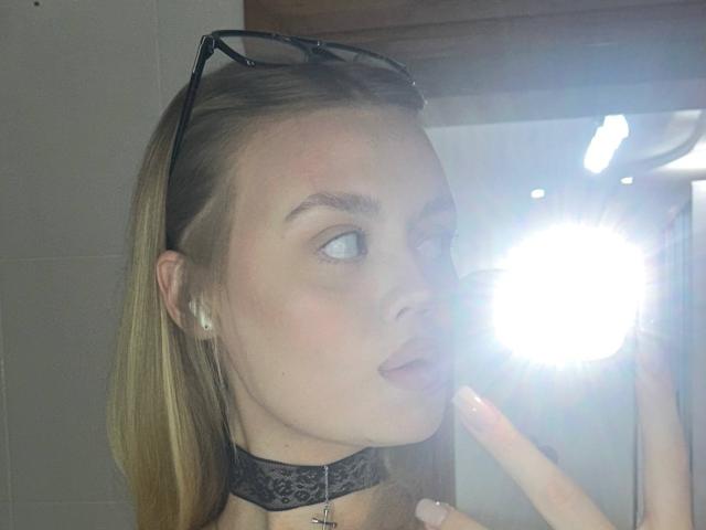 OliviaAzbill with blonde hair, black lace choker, glasses on head, looking to the side, bright flash in front, light skin, pink blush, subtle makeup, reflective surface.