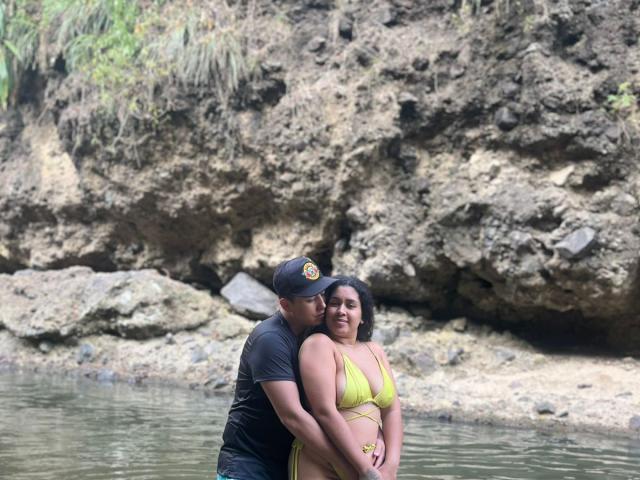 LianaAndAsaff in a yellow bikini stands in shallow water, arms around a guy in a black cap. His hands are on her tits, she has a cute smile.