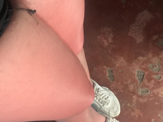 RouseKirryHot's bare ass, showing a small tattoo on the left side, with a white sneaker on the right and a red, textured floor beneath.