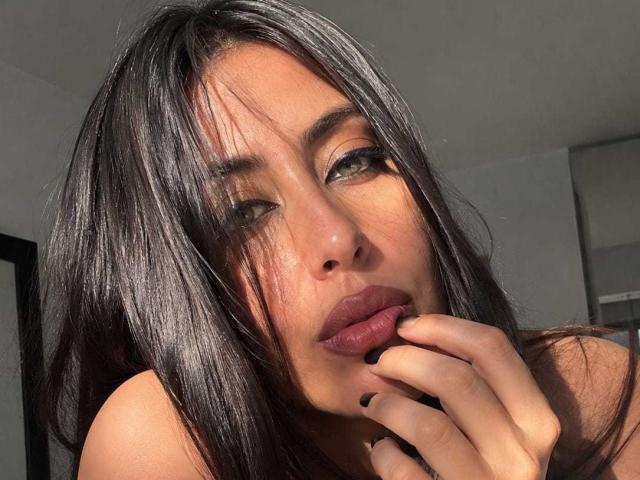 KimyR heeft lang, glanzend zwart haar, volle, roze lippen en donkere wenkbrauwen. Ze raakt haar lippen aan met een vinger en kijkt verleidelijk in de camera. Zonlicht accentueert haar gezicht..